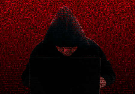 Silhouette of a hacker in a black hood, against the background of computer technology terms....