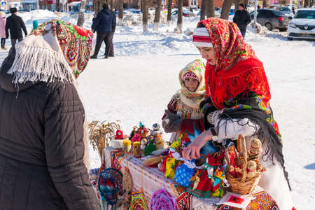 Ufa, Chishmy, Russia, 03.14.2021. The national holiday in Russia is Maslenitsa. Seeing off winter. A girl in a national Russian costume sells souvenirs.のeditorial素材