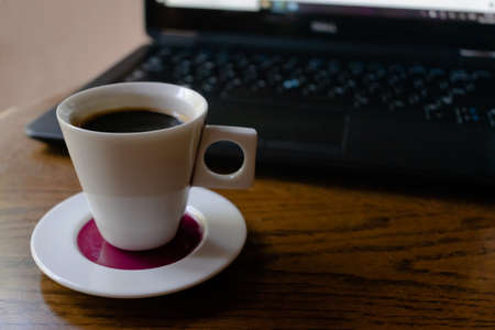 Cup coffee with black computer on brown tableの写真素材