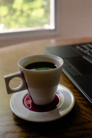 Cup coffee with black computer on brown tableの写真素材