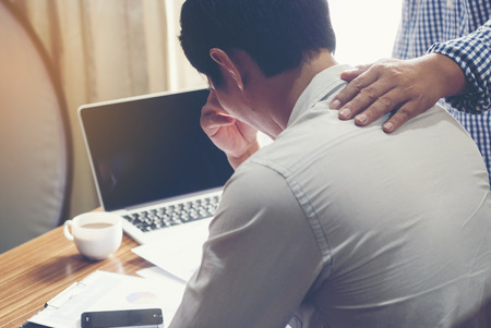 Businessman with hand on shoulder of colleague, consoling businessman suffering from headache in office.の写真素材