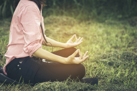 Asian beautiful girl wearing a pink shirt, which is currently sitting on the floor in yoga lawn amid the evening sunlight.の写真素材