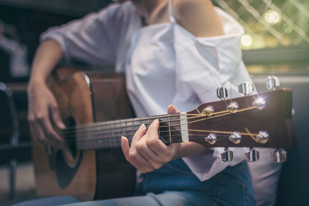 Asian girls wearing white shirts and jeans. She is sitting on a black couch is currently vacationing by playing guitar in a coffee shop.の写真素材
