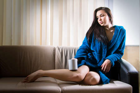 Girl sitting on bed and drinking beverageの写真素材