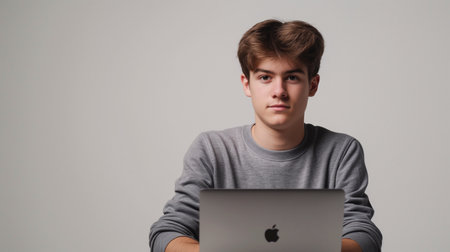 Portrait of a young handsome man with a laptop on a gray backgroundの素材