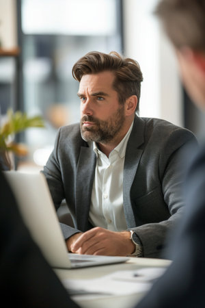 Serious mature businessman looking at laptop screen, sitting at desk in officeの素材