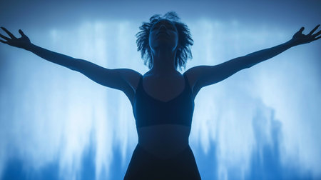 Silhouette of a young woman with arms raised against blue backgroundの素材