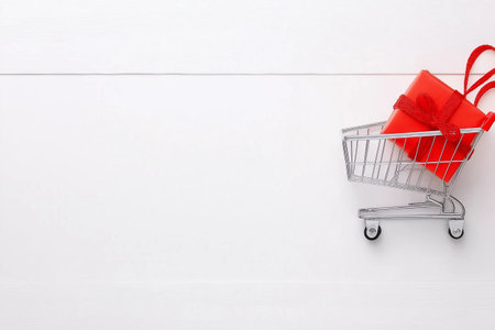 Red gift box in shopping cart on white wooden background. Shopping concept.の素材