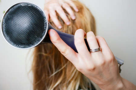 Young blonde woman drying long hair with electric fan. Fan in focusの写真素材