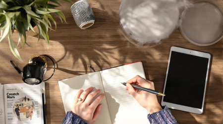 Top view of woman writing in notebook on wooden table with laptop and coffeeの素材