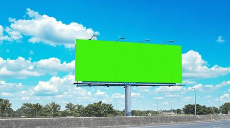 Blank green billboard on the road with blue sky and white clouds background.の素材