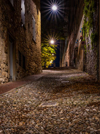 Medieval street that goes up narrow towards Bergamo Alta in the night. Vertical image of nocturnal cityscape.の写真素材