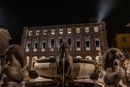 The Sphinx of the Contarini fountain in the foreground in front of the Colleoni library in Piazza Vecchia in Bergamo Alta, historical square of the city of northern Italy, horizontal night imageのeditorial素材