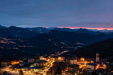The sun rises over a small mountain village still illuminated by night lightsの写真素材