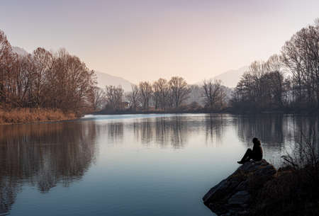 Silhouette of a person sitting on the edge of the river at sunset, Italian landscapeの写真素材