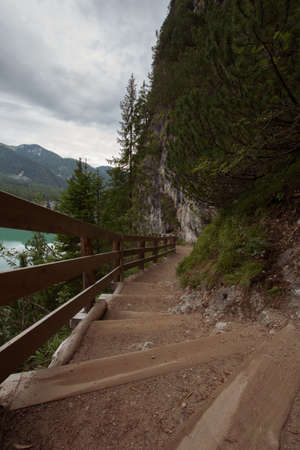 Dirt path to staircase runs along the Braies Lake under a cloudy sky, Trentino Alto Adigeの写真素材