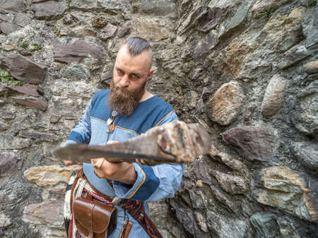 Portrait of a young Viking brandishing an ax in front of a stone wall, portrait set outdoorsの写真素材