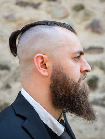 Profile portrait of a man with a long beard and a short haircut in elegant clothes