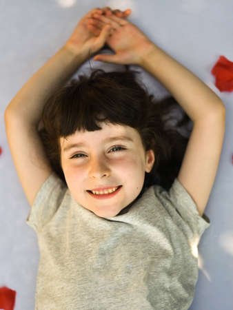 Close up portrait of smiling little girl while rose petals fall on her, vertical portraitの写真素材