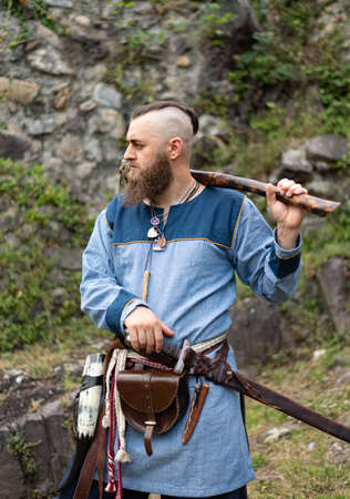 A man in medieval clothes wields an ax in the ruins of an ancient castle, a Viking historical reenactmentの写真素材