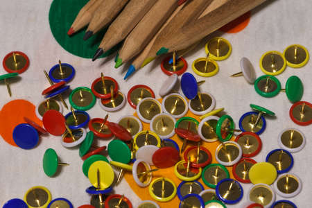 Thumbtacks and colored pencils scattered on a colored plane, horizontal image