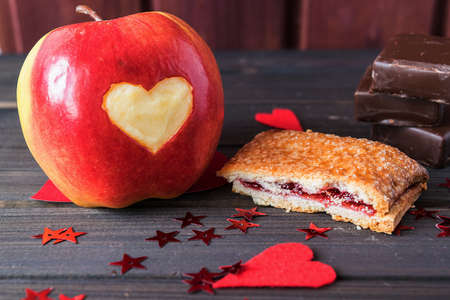 Red apple with heart carved on, cherry pie and chocolate bars decorated with little red stars St.Valentine's Day toned selective focusの写真素材