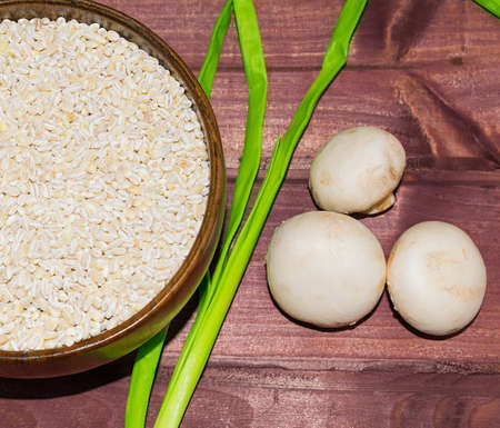 Raw barley, onions and champignons for mushroom soup on wooden planks selective focus tonedの写真素材