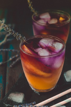 Peach aperol spritz with peach slices and lavender water on wooden desk.