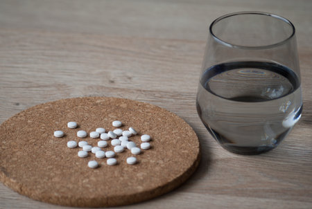 A handful of round white tablets are scattered on the table and a glass of water is nearby.の写真素材