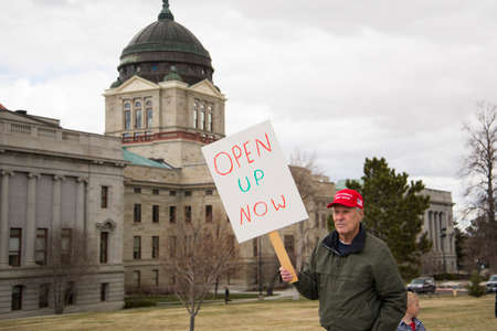 Helena, Montana - April 19, 2020: A senior citizen man protesting wearing a red Make America Great Again hat holding a sign saying to open up the government Coronavirus shutdown.のeditorial素材