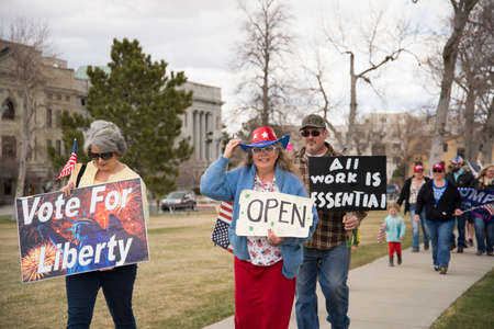 Helena, Montana - April 19, 2020: A woman wear an red white blue American flag costume at a protest to open the government shutdown. A man and women holding sign that all work is essential.のeditorial素材