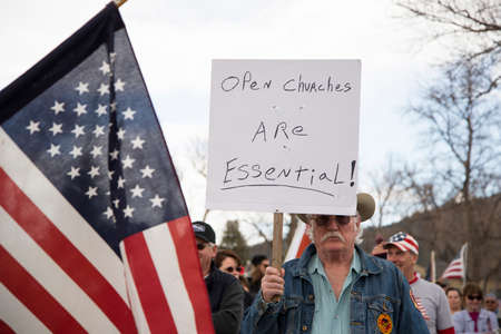 Helena, Montana - April 19, 2020: Marine Corps veteran protesting and holding sign that churches are essential again the government shutdown with an American flag in the foreground.のeditorial素材