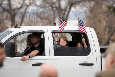 Helena, Montana - April 19, 2020: Children girls holding and waving American flag from a vehicle at...