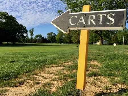 Golf course cart arrow directional sign towards paved path for player vehicle. Nature landscape fairway trees in background. Green sign on yellow post white lettersの写真素材