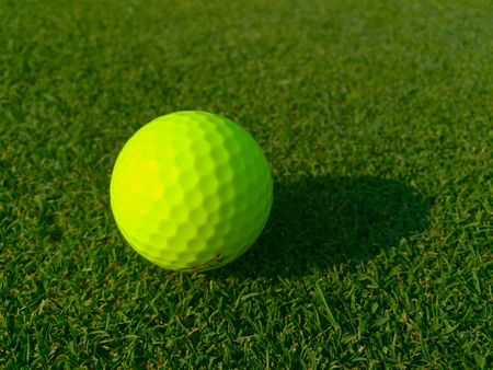 Isolated bright green golf ball site on golf course grass waiting for player to putt into hole for par score. Morning sunrise shadow cast on fairway. Low Angleの写真素材