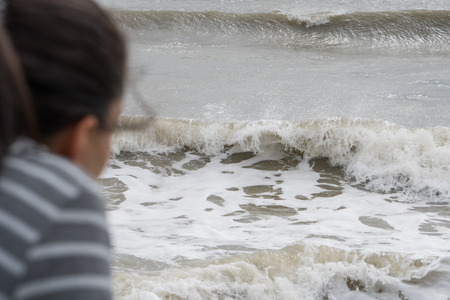 Young woman at the beach watches the crashing waves along the coastの写真素材