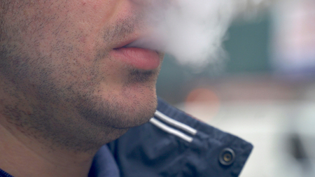 Young hipster millennial male exhale e-cigarette vaporizor smoke outside on urban city street during day time.の写真素材