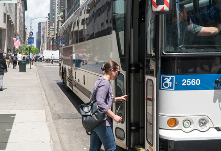 New York City, Circa 2017: Woman enters MTA Bus on Manhattan 5th avenue during day time commute. People use public transportation to navigate through heavy traffic streetsのeditorial素材