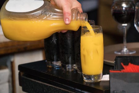 Bartender pour orange juice mixed cocktail drink into tall glass with ice to serve at restaurant bar for customer order. Mix with champagne for mimosa traditional brunch drinkのeditorial素材