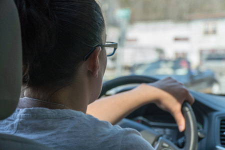 Over the shoulder POV young woman driving a car on a busy urban street road during the day time.の写真素材