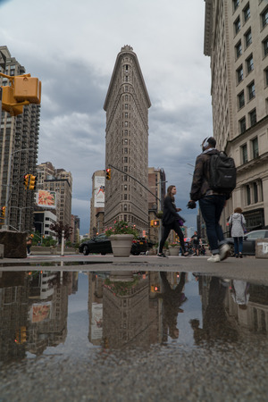 New York City, Circa 2019: Flat Iron building wide exterior establishing shot street view during morning rush hour commute. People walk along side walk with building reflection in rain puddleのeditorial素材