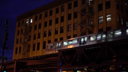 Chicago loop train passing by downtown apartment building at night on overhead elevated track through city. Public transportation to city nightlife の写真素材