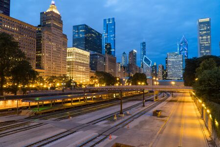 Evening twilight exterior skyline shot of downtown Chicago at night with building cityscape illuminating the dark sky view over train track rail yard for loop transit systemの写真素材