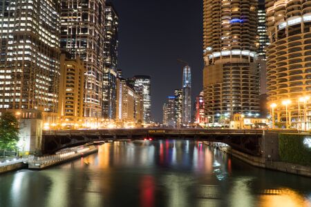 Night time exterior establishing shot overlooking Chicago river front area with skyline illuminated in dark sky reflecting off water in beautiful scene bridge road overpass with car trafficの写真素材