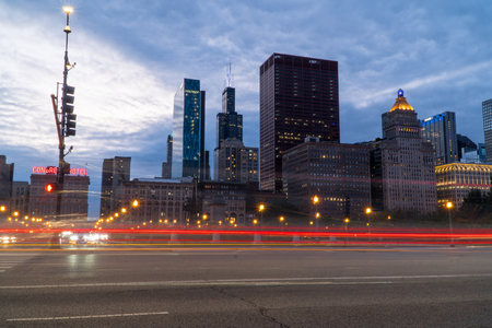 Chicago, IL - Circa 2019: Night time establishing shot of downtown Chicago skyline long exposure light trails of cars passing through busy intersection surrounding city.のeditorial素材