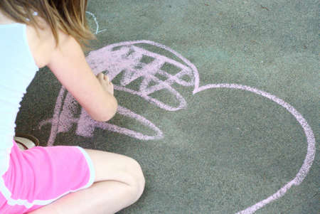 Girl playing with chalk and drawing a heartの写真素材