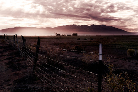 Sunset with a rusty fence and a farm in the backgroundの写真素材