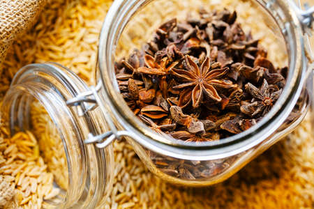 Jar with star anis placed on bag full of anis seeds