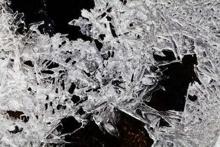 Closeup of crystals of ice on the ground melting on natural black backgroundの写真素材