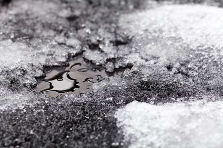 Tiny puddle of melting snow on asphalt